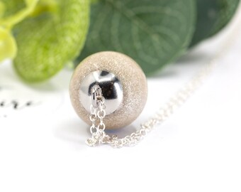 May include: A silver chain necklace with a large, round, sparkly, beige pendant.