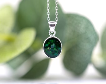 May include: A silver chain necklace with a round green pendant. The pendant is filled with green glitter and small white flecks.