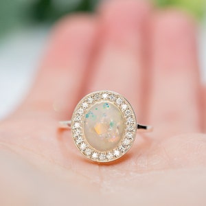 May include: A silver ring with a white opal gemstone surrounded by a halo of small diamonds.
