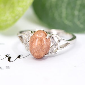 May include: A silver ring with a brown oval gemstone and a delicate heart-shaped design. The ring is set with small clear stones.
