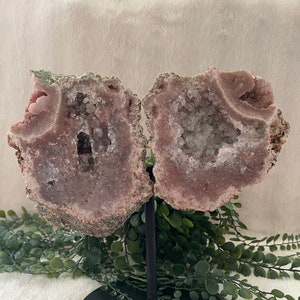 May include: A large pink amethyst geode with clear quartz crystals inside, displayed on a black metal stand.