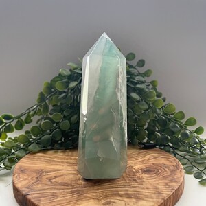 May include: A green fluorite crystal point on a heart-shaped wooden stand. The crystal is clear with green and white swirls.