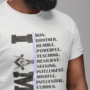May include: A white t-shirt with a black graphic design that spells out "IM" with a Masonic symbol. The text reads "Man, Brother, Humble, Powerful, Teaching, Resilient, Seeking, Intelligent, Mindful, Influential, Curious, Kingly."