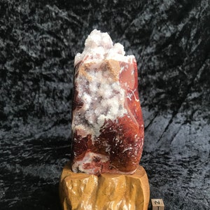 Pode incluir: Uma geoda de ágata vermelha e branca com um aglomerado de cristais brancos em um suporte de madeira. O suporte é etiquetado com "N.T. 10CM".