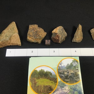 以下が含まれることがあります： 1cmの定規をスケールにした、不規則な形をした、ざらざらした質感の茶色と緑の石が5つあります。