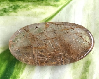 May include: A clear quartz crystal with golden rutilated inclusions. The crystal is oval shaped and polished smooth.