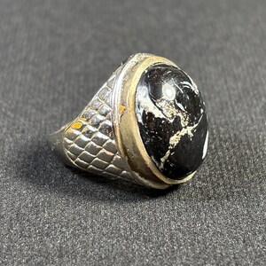 May include: A silver ring with a black and white oval gemstone set in a silver bezel. The band of the ring has a textured, checkered pattern.