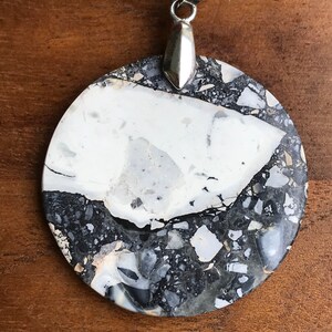 May include: A round, white and black marbled pendant with a silver bail. The pendant is made of a natural stone with a unique pattern.