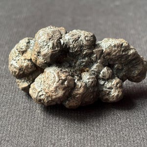 May include: A close-up of a cluster of pyrite, also known as fool's gold, with a metallic, textured surface. The mineral has a dark, brownish-gold color and is set against a gray background. The pyrite cluster is a natural, geological specimen.