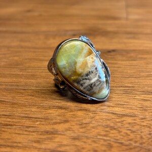 Può includere: Un anello d'argento con una grande pietra preziosa ovale di colore verde e marrone incastonata al centro.