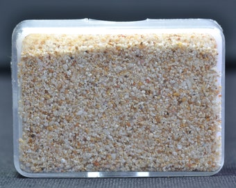 Könnte beinhalten: Ein durchsichtiger Plastikbehälter gefüllt mit kleinen, weißen und beigefarbenen Sandkörnern.