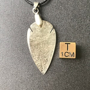 May include: A clear, teardrop-shaped pendant with a silver-colored bail hangs from a black cord. The pendant has a speckled, textured appearance. A 1 cm square is next to the pendant.