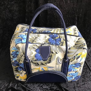 Op de afbeelding: Een reistas met een blauwe en witte bloemenprint, een donkerblauwe handvat en afwerking. De tas heeft een groot compartiment en een kleiner vakje aan de voorkant.