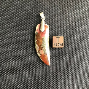 Könnte beinhalten: Ein Anhänger aus rotem, grünem und weißem Achat, in Form eines Zahns, mit einer silbernen Öse. Der Anhänger ist etwa 2,5 cm lang.