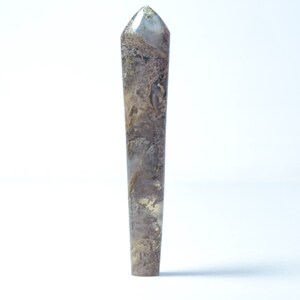 May include: A tall, slender crystal point with a textured surface. The crystal features a mix of brown, gray, and gold tones, with a pointed tip. The crystal is standing upright against a white background. This is a decorative item.