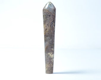 May include: A tall, slender crystal point with a textured surface. The crystal features a mix of brown, grey, and gold tones, with a pointed tip. The crystal is standing upright against a white background. This is a decorative item.