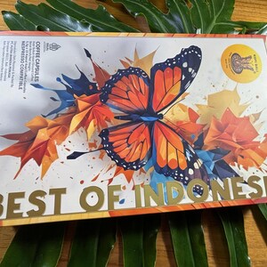 Puede incluir: Una caja rectangular de c&aacute;psulas de caf&eacute; con un dise&ntilde;o de mariposa. La mariposa es naranja, negra y blanca, sobre un fondo de formas geom&eacute;tricas naranjas, amarillas y azules. Las palabras "BEST OF INDONESIA" est&aacute;n en letras doradas.