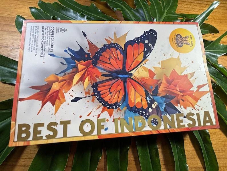 Puede incluir: Una caja rectangular de c&aacute;psulas de caf&eacute; con un dise&ntilde;o de mariposa. La mariposa es naranja, negra y blanca, sobre un fondo de formas geom&eacute;tricas naranjas, amarillas y azules. Las palabras "BEST OF INDONESIA" est&aacute;n en letras doradas.