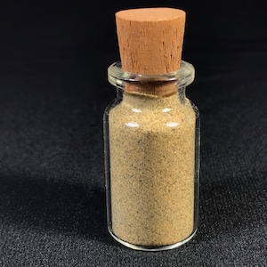 May include: A small glass bottle with a cork stopper filled with a light brown sand-like substance.