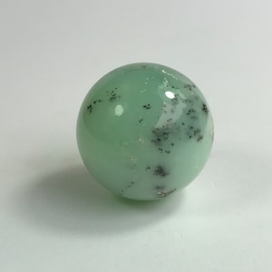 Puede incluir: Una esfera lisa de color verde con motas negras. La esfera está hecha de piedra pulida.