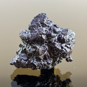 Op de afbeelding: Een donker, getextureerd mineraal specimen met een metallic uiterlijk. Het oppervlak is diep, reflecterend zwart met lichtere, zilverachtige highlights. De vorm is onregelmatig en rotsachtig, met een ruwe, ongelijke textuur.