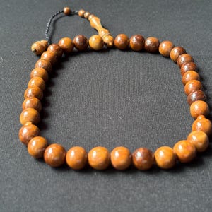 May include: A string of prayer beads made from polished, round wooden beads. The beads are a warm brown colour, strung together with a black cord. The beads are arranged in a loop.