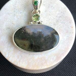 Könnte beinhalten: Ein silberner Anhänger mit einem grünen Achat-Stein und zwei kleineren grünen Edelsteinen. Der Anhänger befindet sich auf einem weißen Hintergrund.