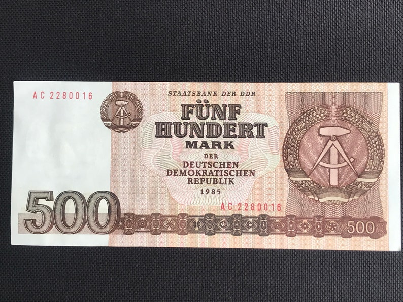 May include: A 500 Mark banknote from the German Democratic Republic, dated 1985. The note features a red and brown design with the text "F&uuml;nf Hundert Mark" and the words "Der Deutschen Demokratischen Republik" in the center. The note also features a compass and hammer symbol.