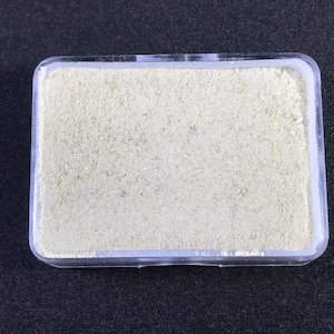 Puede incluir: Un pequeño recipiente de plástico transparente lleno de polvo beige claro.