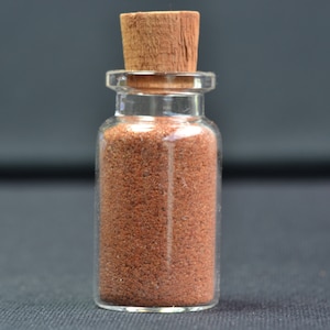 Peut inclure: Une petite bouteille en verre avec un bouchon en liège remplie d'une poudre brun rougeâtre.
