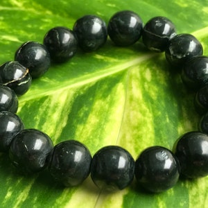 May include: A black gemstone bracelet with round beads. The bracelet is on a green leaf background.