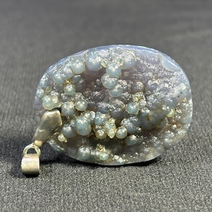 May include: A silver pendant with a light purple and blue agate stone. The stone has a unique pattern of small, round, blue and white inclusions.