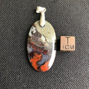 Può includere: Un ciondolo d'argento con una pietra ovale marrone, rossa e grigia. La pietra ha un motivo marmoreo. Il ciondolo è lungo 2,5 cm.