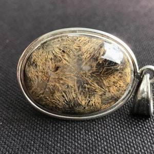 Puede incluir: Un colgante de plata con una piedra ovalada transparente que contiene una formación de cristal marrón y blanco.