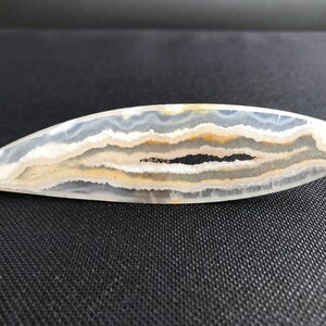 Peut inclure: Une tranche d'agate blanche avec des bandes brunes et noires. L'agate est polie et a une forme ovale lisse.