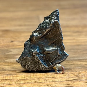 Puede incluir: Un colgante de plata con forma de roca irregular con un pequeño bucle para una cadena.