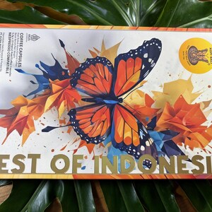 Puede incluir: Una caja de c&aacute;psulas de caf&eacute; con un dise&ntilde;o colorido que presenta una mariposa y el texto "BEST OF INDONESIA". La caja tiene un sello dorado que dice "KOPI BALI". El fondo tiene formas geom&eacute;tricas naranjas, azules y amarillas.