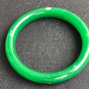 Puede incluir: Un brazalete de jade verde. El brazalete es liso y pulido.