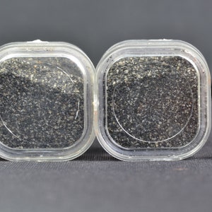 Puede incluir: Dos recipientes de plástico transparente llenos de arena negra. Una regla de 1 cm se incluye para la escala.