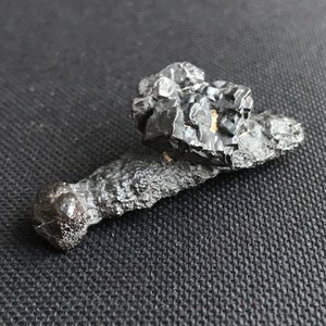 Puede incluir: Un espécimen mineral negro, rugoso y de forma irregular con un acabado brillante y metálico.