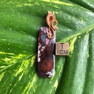May include: A brown and white agate pendant with a copper wire wrap. The pendant is approximately 1 inch in length. A 1 cm ruler is included for size reference.