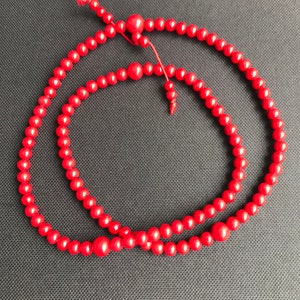 May include: A red beaded necklace with a knotted tassel. The beads are round and smooth, and the necklace is strung on a thin cord.