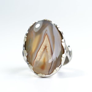 Puede incluir: Un anillo de plata con una piedra de ágata marrón y blanca engastada en un engaste de plata texturizado.