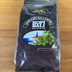 Könnte beinhalten: Ein dunkler Beutel Kopi Bali Arabica Kaffee mit dem Text "100% Pure Bali Coffee". Auf dem Beutel steht auch "Kopi Biji/Roasted Bean" und "Berat Bersih 250g". Der Beutel hat ein Bild eines Berges und einiger Blätter.