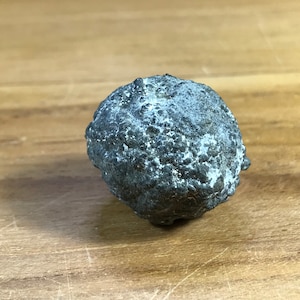 May include: A dark gray, round, textured rock with a rough surface.