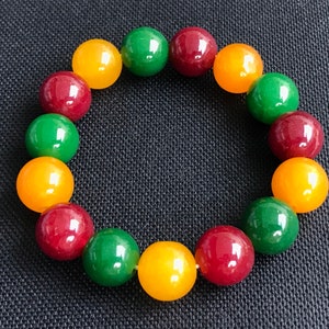 Puede incluir: Un brazalete hecho de cuentas redondas en colores rojo, verde y amarillo.