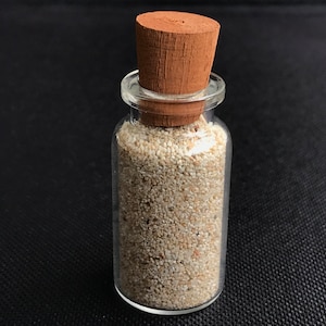 May include: A small glass bottle with a cork stopper filled with white sand.