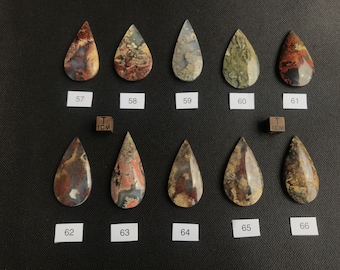 Könnte beinhalten: Zwölf tropfenförmige Achat-Cabochons in verschiedenen Brauntönen, Rot- und Grüntönen. Die Cabochons sind in zwei Reihen zu sechs angeordnet, mit einem Lineal als Maßstab. Das Lineal ist mit "1 CM" beschriftet.