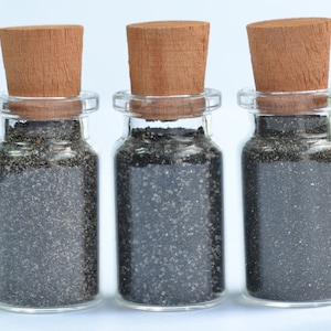 May include: Three small glass bottles with cork stoppers filled with black sand.