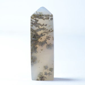 May include: A white and gray agate crystal point with brown and black inclusions. The crystal is polished and has a pointed tip.